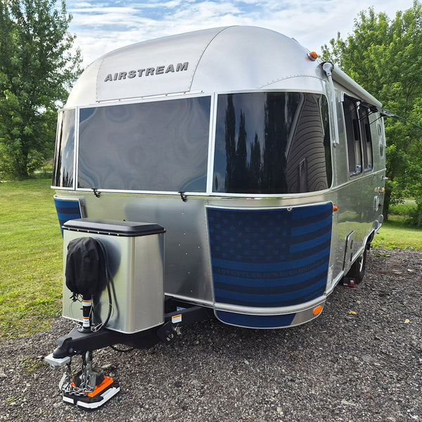 Airstream trailer parked on a gravel surface with trees in the background
