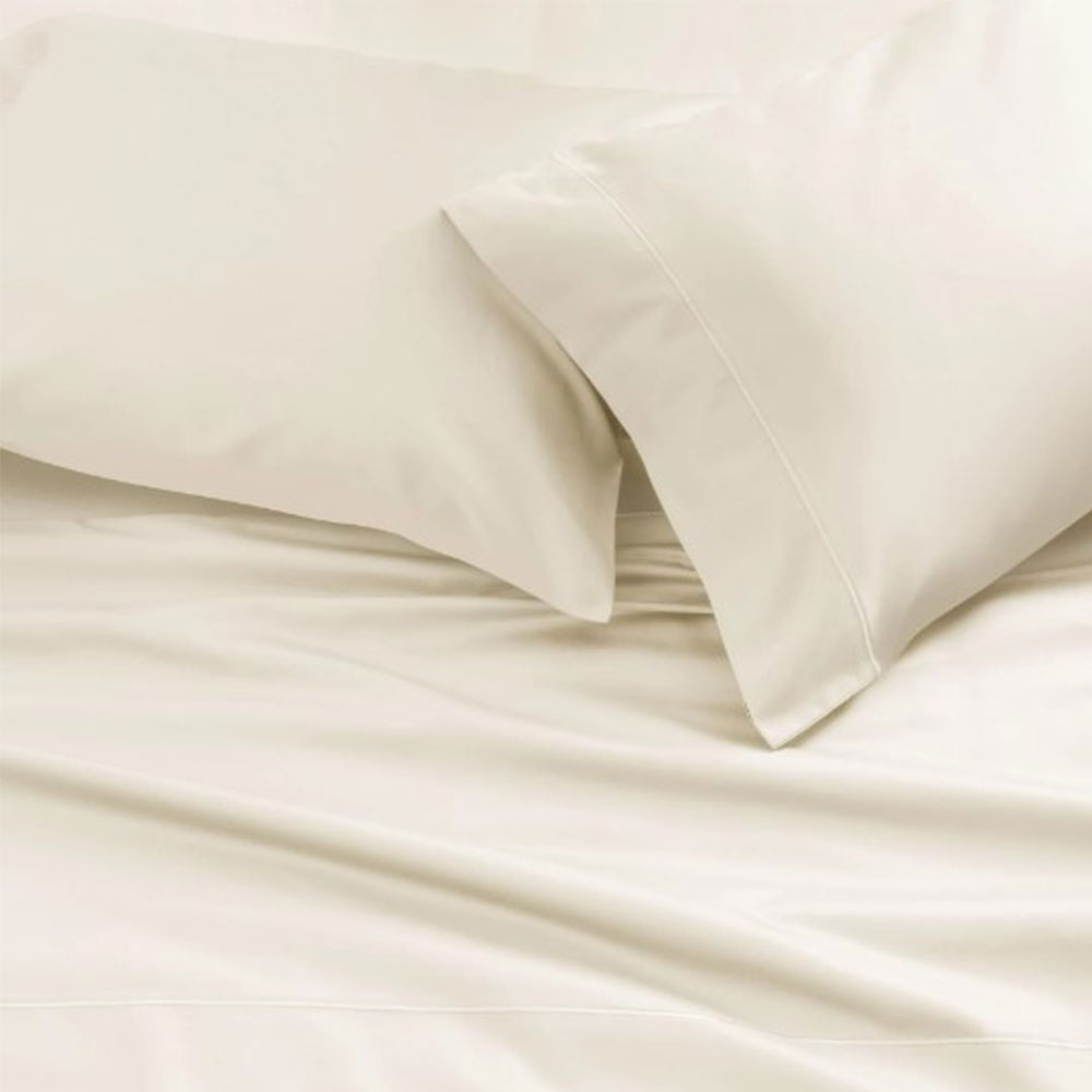 Two ivory-colored pillows in luxurious Cotton Sateen 500 Thread Count Pillowcases and a matching bed sheet are neatly arranged on a bed, creating a soft and inviting appearance.