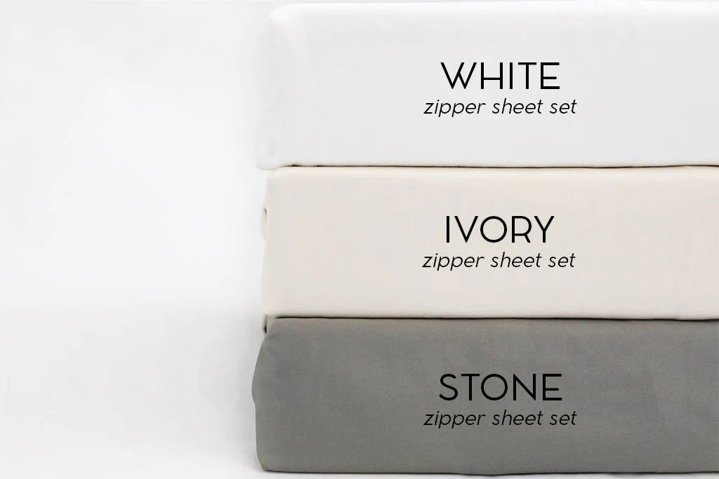 Three folded Airstream RV Fit Beddy’s ZipBase Sheets for Flying Cloud Travel Trailers stacked vertically—ideal for Airstream beds or RV-sized mattresses. From top to bottom: white, ivory, and stone gray, each labeled with its color and the “ZipBase Sheet Set” text on the front.