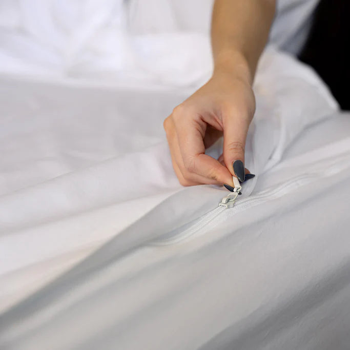 A person with painted nails zips up Airstream RV Fit Beddy’s ZipBase Sheets for Classic Travel Trailers, with crisp white bedding visible in the background.